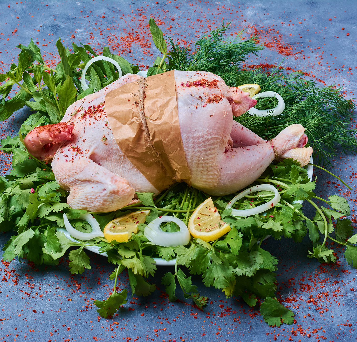 Raw chicken with herbs on a wooden board on blue background دجاج كاملة - الصورة 1