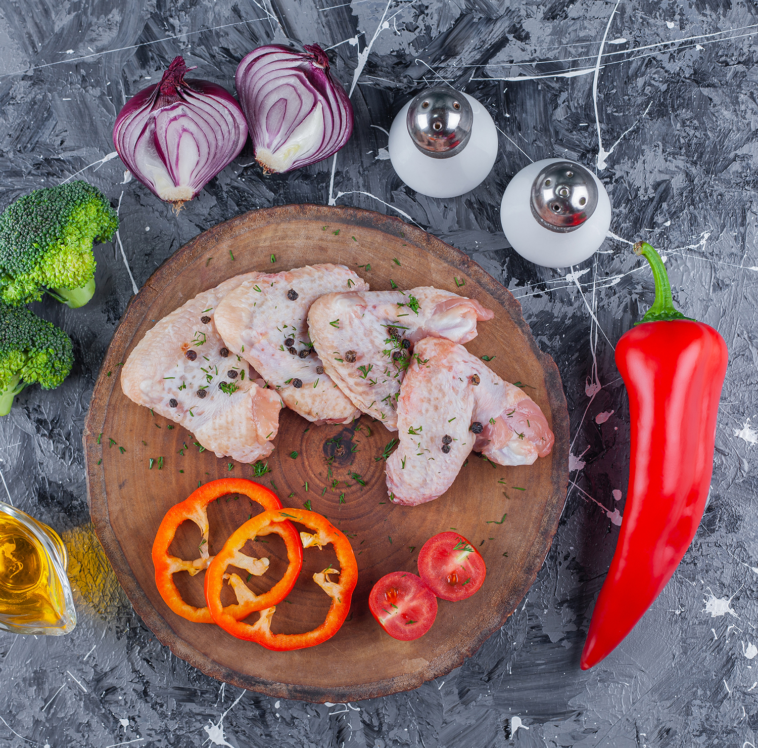 Sliced bell pepper, tomatoes and wing on a board next to onion, salt and pepper, on the blue background جناح فراخ - الصورة 1